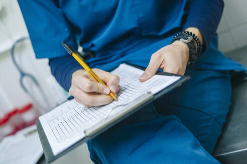 Female nurse writing medical report while sitting in hospital - DGOF01905
