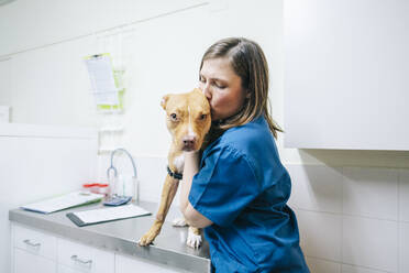 Female nurse kissing dog at operating table in veterinarian clinic - DGOF01906