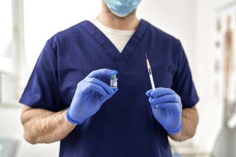 Male doctor in medical scrub holding COVID-19 vaccine and syringe stock photo