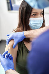 Female patient taking COVID-19 vaccination on arm wearing protective face mask at clinic - ABIF01327