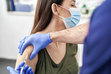 Mature female patient taking vaccination on arm while wearing protective face mask at clinic - ABIF01328