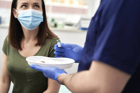 Female patient with face mask discussing with male doctor before taking vaccination against COVID-19 stock photo