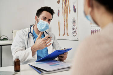 Male doctor with protective face mask talking with patient in clinic - ABIF01350