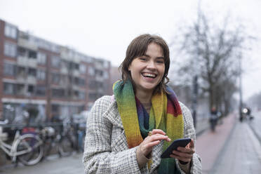 Lachende Frau, die ein Mobiltelefon benutzt, während sie gegen den Himmel steht - AXHF00154