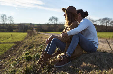 Heterosexuelles Paar sitzt bei Sonnenuntergang auf einem Feld - VEGF03851