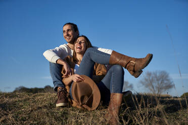 Lachendes Paar sitzt auf dem Land gegen den blauen Himmel bei Sonnenuntergang - VEGF03853