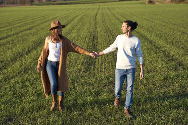 Heterosexuelles Paar, das sich an den Händen hält und sich beim Spazierengehen auf einer Grünfläche ansieht - VEGF03861