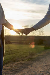Heterosexuelles Paar hält sich bei Sonnenuntergang an den Händen - VEGF03869