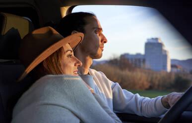 Mann fährt Auto, während sich eine Frau bei Sonnenuntergang umarmt - VEGF03874