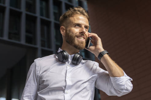 Geschäftsmann schaut weg, während er im Freien mit seinem Handy telefoniert - BOYF01776