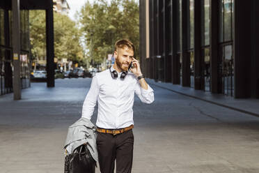 Businessman talking on mobile phone while walking on footpath - BOYF01780