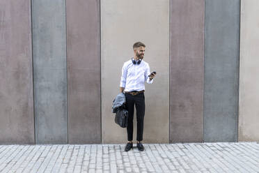 Geschäftsmann, der ein Smartphone benutzt, während er an der Wand steht - BOYF01788