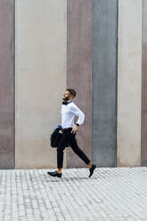 Businessman holding briefcase while running on footpath - BOYF01791