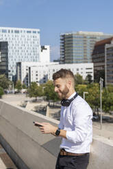 Mid adult businessman using mobile phone while standing on bridge in city - BOYF01799