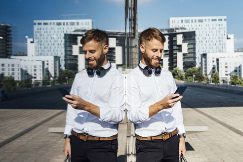 Geschäftsmann, der ein Mobiltelefon benutzt, während er an einer Glaswand steht - BOYF01803