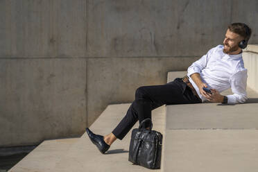 Businessman using mobile phone while relaxing on steps - BOYF01815