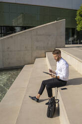 Geschäftsmann, der ein digitales Tablet benutzt, während er mit einer Aktentasche auf einer Treppe sitzt - BOYF01817