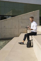 Mid adult businessman using digital tablet while sitting on steps - BOYF01818