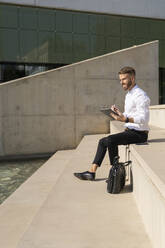 Mittelgroßer Geschäftsmann, der auf einer Treppe sitzend ein digitales Tablet benutzt - BOYF01818