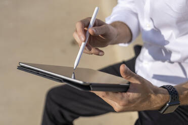 Businessman using digital table while sitting outdoors on sunny day - BOYF01822