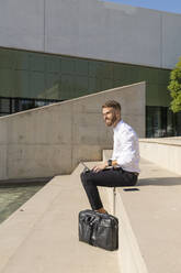 Businessman using digital tablet while sitting on steps during sunny day - BOYF01824