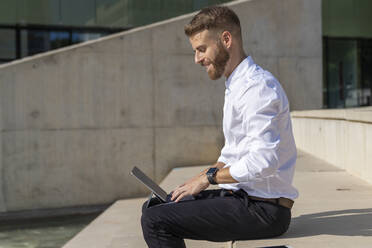 Smiling entrepreneur using digital tablet while sitting on steps - BOYF01826