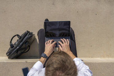 Geschäftsmann, der an einem digitalen Tablet arbeitet, während er mit einer Aktentasche auf den Stufen sitzt - BOYF01829