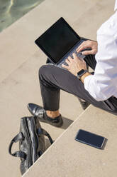 Geschäftsmann, der ein digitales Tablet benutzt, während er an einem sonnigen Tag auf einer Treppe sitzt - BOYF01831