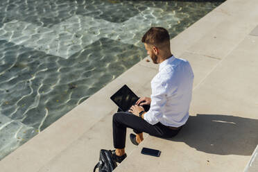 Mittlerer erwachsener Geschäftsmann, der auf einer Treppe sitzend an einem digitalen Tablet arbeitet - BOYF01832