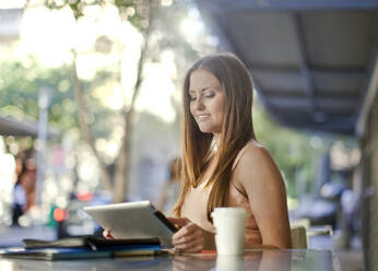 Unternehmerin, die in einem Straßencafé sitzt und ein digitales Tablet benutzt - AJOF01009