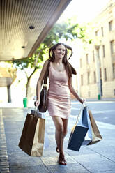 Shopaholic woman running on footpath with bags - AJOF01012