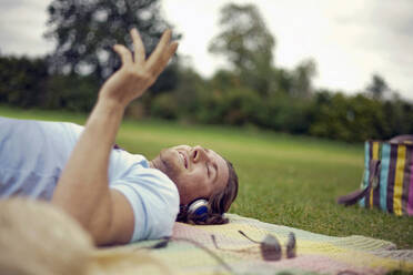 Young man listening music while lying down at park - AJOF01015