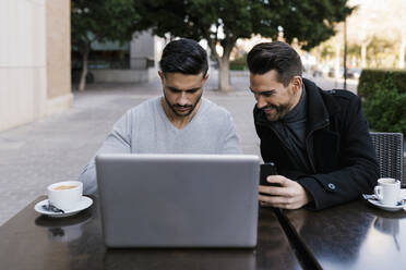 Männliche Freunde mit Laptop, die Kaffee trinken, während sie in einem Straßencafé in der Stadt sitzen - EGAF01705