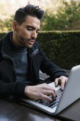 Gut aussehender Mann, der einen Laptop benutzt, während er am Tisch sitzt - EGAF01708
