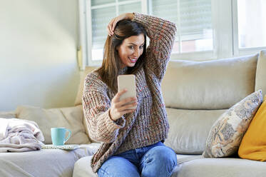 Lächelnde Frau nimmt Selfie auf Sofa zu Hause - KIJF03588