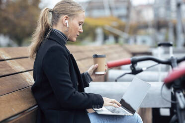 Frau benutzt Laptop und hält Kaffeetasse am Fahrrad - JSRF01390