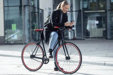 Lächelnde Frau, die ein Mobiltelefon benutzt und sich auf ein Fahrrad stützt - JSRF01398