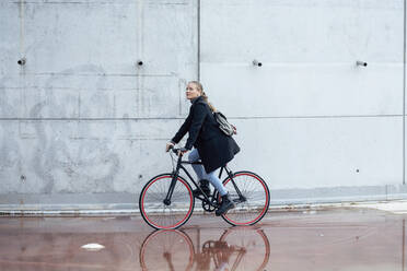Woman doing cycling on wet road by wall - JSRF01402