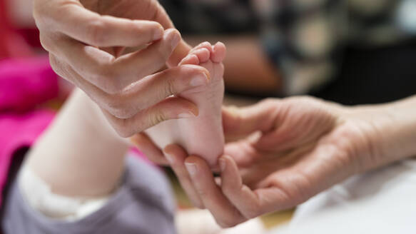 Eine Physiotherapeutin behandelt manuell den Fuß eines Säuglings - CAVF92790
