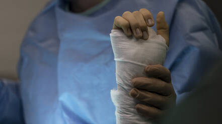 Ein Chirurg hält das Handgelenk eines operierten Patienten im Operationssaal - CAVF92816