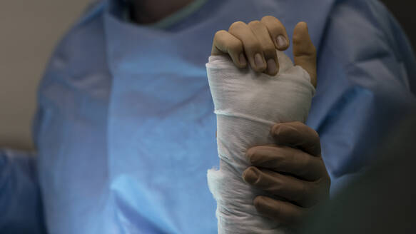 A surgeon holds the wrist of an operated patient in the operating room - CAVF92816