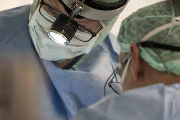 Gesicht eines Chirurgen mit einer Stirnlampe während einer Operation - CAVF92819
