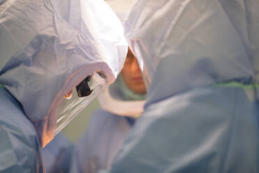 Three Surgeons are in the operating room in protective surgical suits - CAVF92823