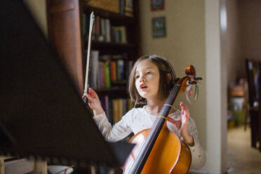 Ein kleines Mädchen, das ein Cello in der Hand hält, hebt den Bogen, um sich auf das Spiel vorzubereiten - CAVF92959