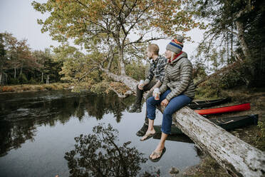 Couple sit on tree branch drinking beer while canoeing on river, Maine - CAVF93052