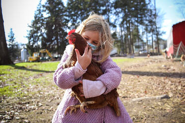 Girl holding chicken on a farm wearing a mask - CAVF93102