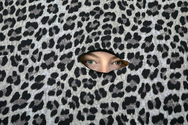 Die Augen eines Teenagers blicken durch ein Loch im Leopardenmuster - PSTF00850