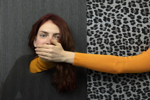 Studio shot of female hand covering mouth of young redhead woman - PSTF00862