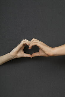 Studioaufnahme einer männlichen und einer weiblichen Hand, die eine Herzform bilden - PSTF00870