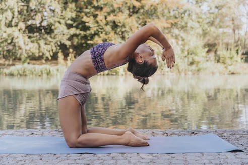 Sportlerin mit verschränkten Händen, die auf einer Matte sitzend im Park Yoga praktiziert - MFF07112